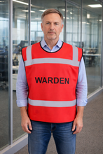 Load image into Gallery viewer, Man wearing a red 'WARDEN' safety tabbard style vest in an office setting

